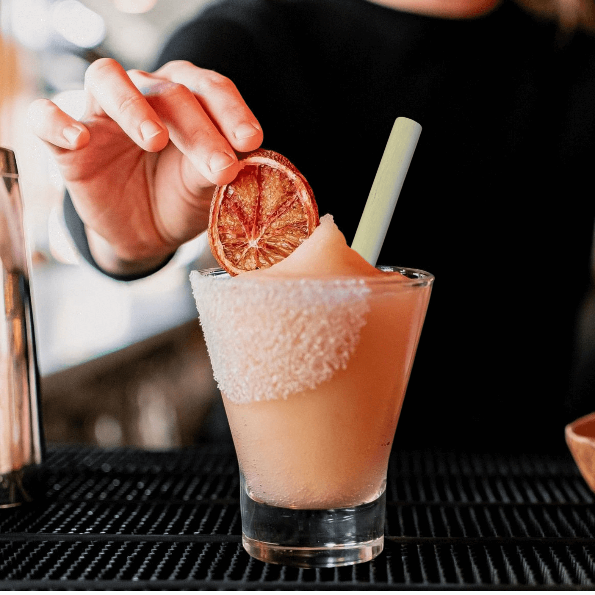 Frozen paloma with hand placing grapefruit in drink with cocktail reed straw