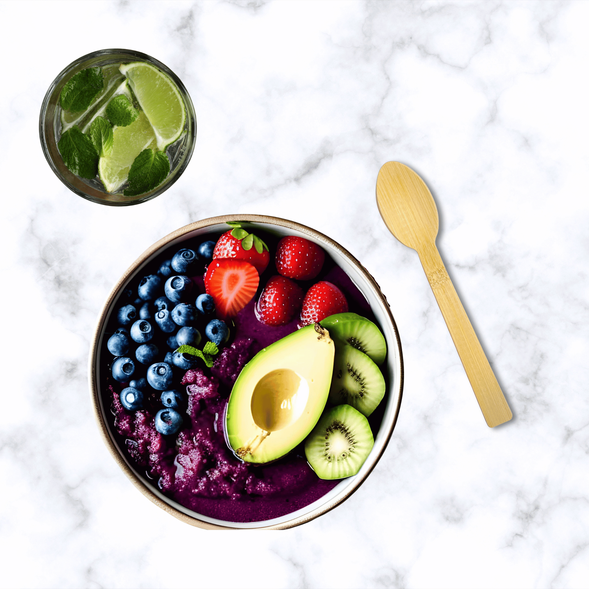 A refreshing acai bowl topped with sliced strawberries, blueberries, kiwi, and half an avocado, served next to an unwrapped bamboo spoon from Holy City Straw Co. A glass of lime-infused water with mint leaves is placed on a marble surface alongside the bowl.
