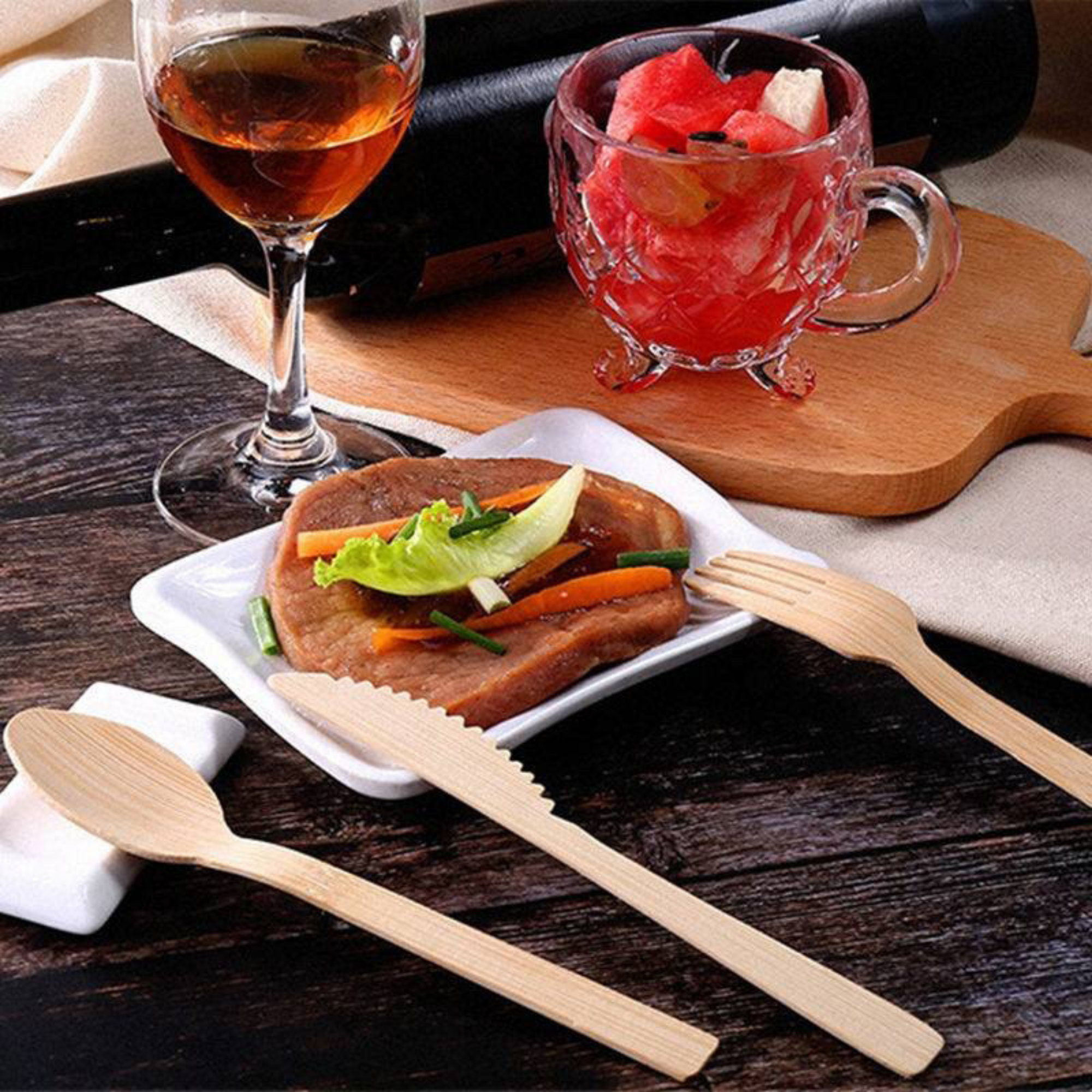 Environmentally-friendly bamboo cutlery set by Holy City Straw Co. displayed on a bamboo cutting board, with a fork, knife, and spoon visible next to slices of fresh broccoli and tomato. Icons below emphasize the utensils' features: Made from Bamboo, 100% Biodegradable, Liquid/Heat Resistant, and Zero Waste