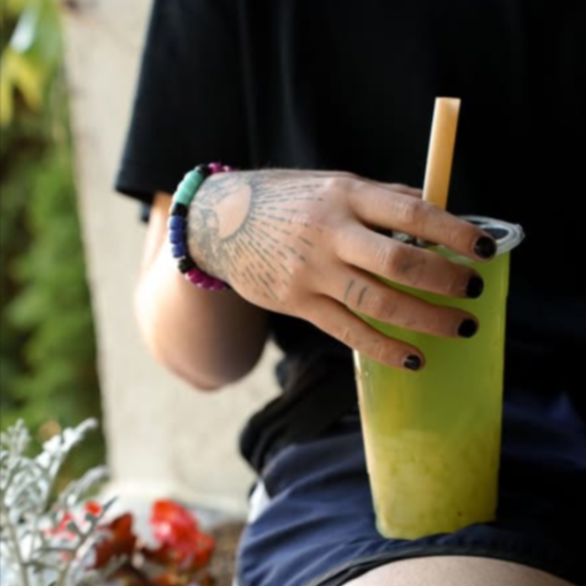 Tattooed hand holding a green bubble tea with a bamboo fiber boba straw, representing eco-conscious lifestyle and sustainable drinkware choice.