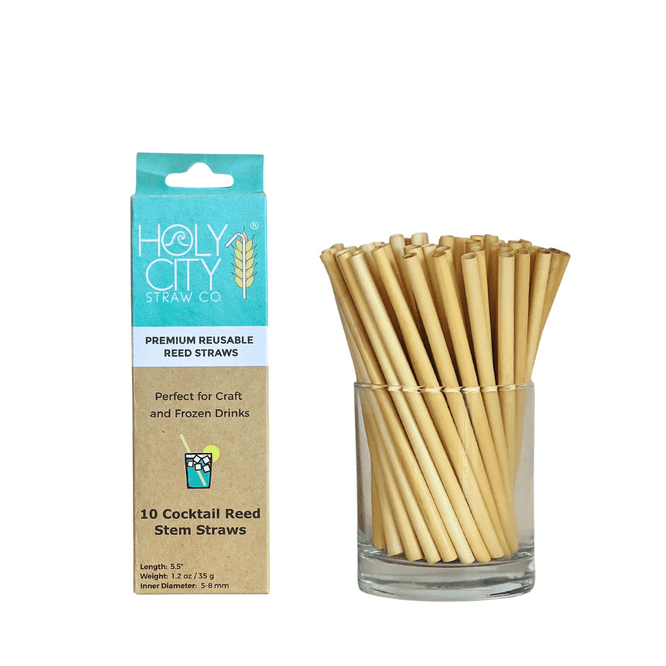 Image of a package and a glass jar containing Holy City Straw Co.'s 5.5-inch reusable cocktail reed straws. The package is light blue and brown, displaying the brand's logo and stating 'Premium Reusable Reed Straws,' ideal for craft and frozen drinks. The jar next to the package is filled with the natural reed straws, showcasing their eco-friendly design.