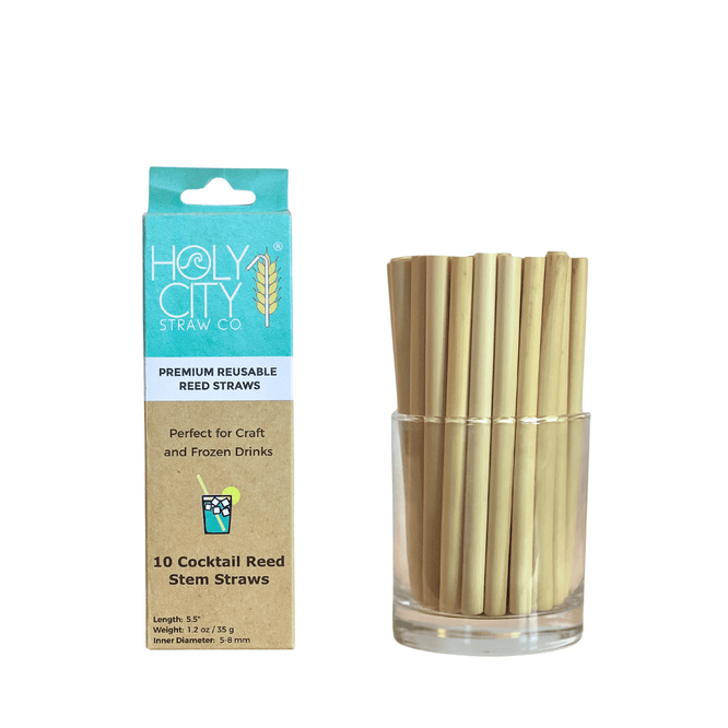 Image of a package and a glass jar containing Holy City Straw Co.'s 5.5-inch reusable cocktail reed straws. The package is light blue and brown, displaying the brand's logo and stating 'Premium Reusable Reed Straws,' ideal for craft and frozen drinks. The jar next to the package is filled with the natural reed straws, showcasing their eco-friendly design.