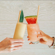 Hand cheersing citrus and watermelon cocktails with reed stem straws