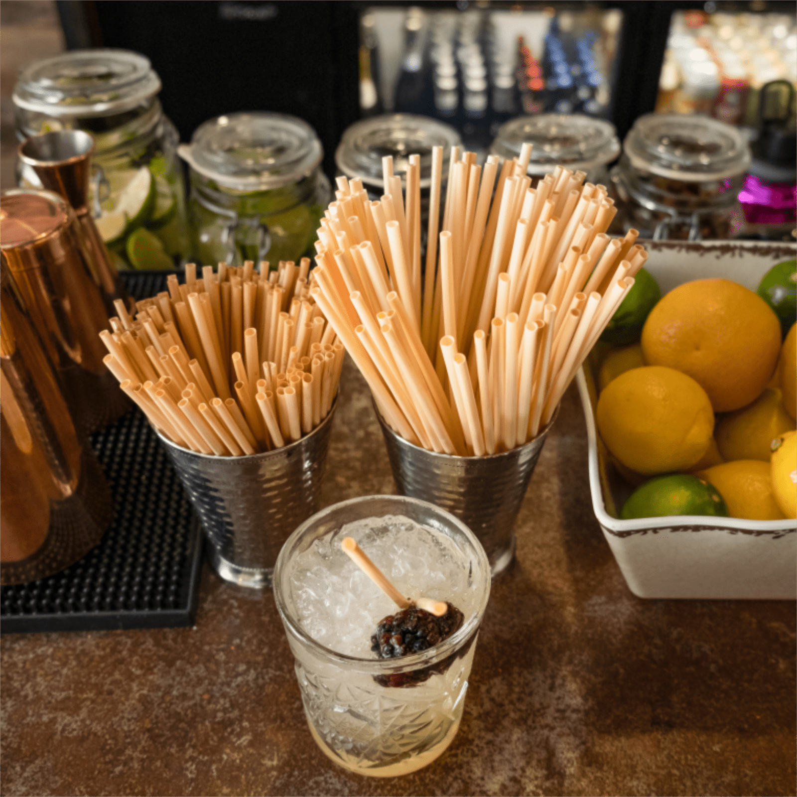 Holy City Straw Company Tall and Cocktail Straws in a straw holder at Bar with Drink alongside other bar top accessories