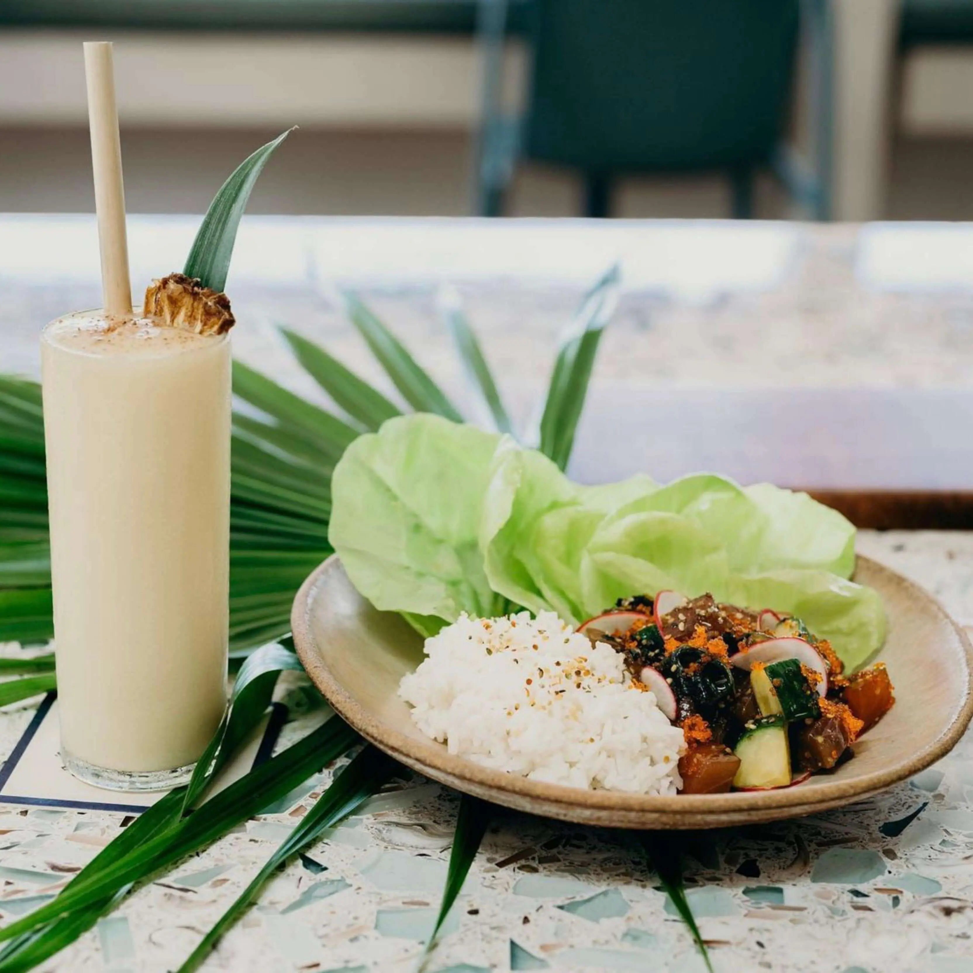 Pina colada with reed stem straw next to plate of food